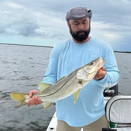 Person holding a large fish on a boat with cloudy sky in the background.