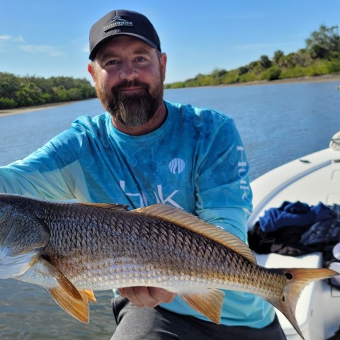 Man on a boat holding a fish with water and a woman in the background.