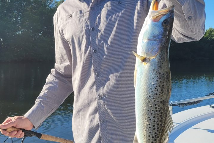 Man on a boat holding a speckled fish with a fishing rod.
