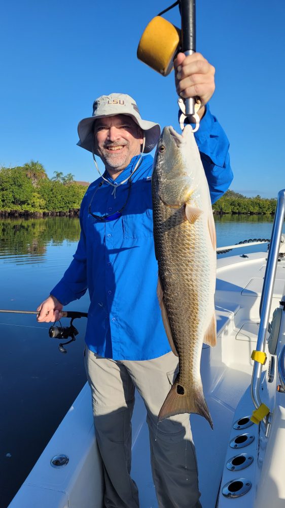 Man on boat holding a large fish, wearing a blue shirt and sunhat.