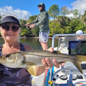 Person in cap holding a fish on a boat with others fishing in the background.