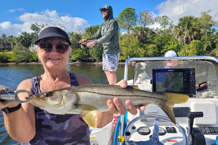 Person in cap holding a fish on a boat with others fishing in the background.