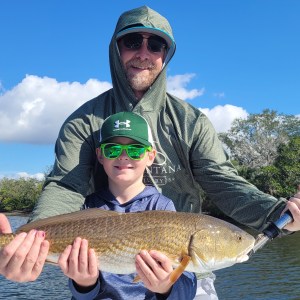 Two people holding a large fish by a river on a sunny day.