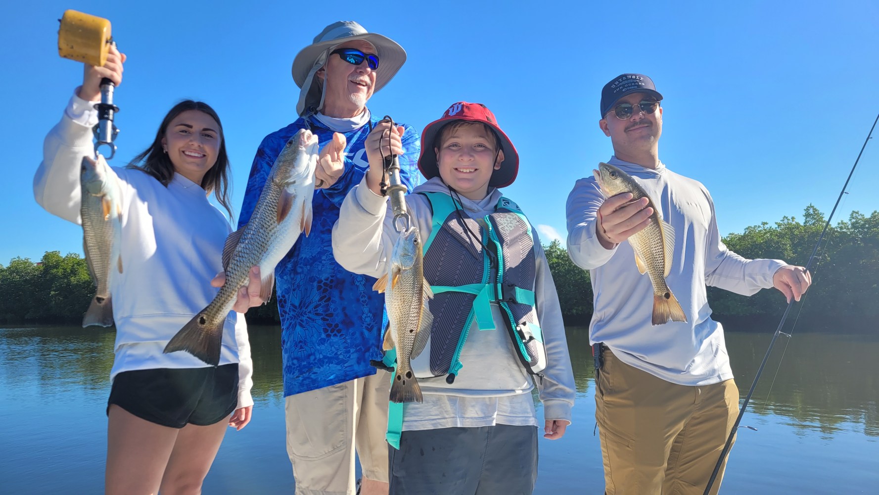 Four people standing on a boat holding fish, smiling against a clear blue sky.