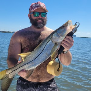 Man holding a large fish on a boat with water and blue sky in background.