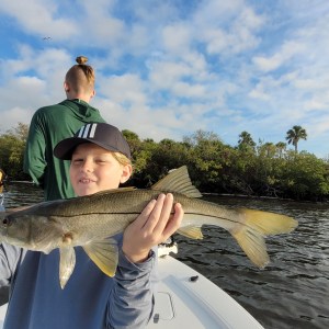 Person holds fish on boat, another person in background facing away.