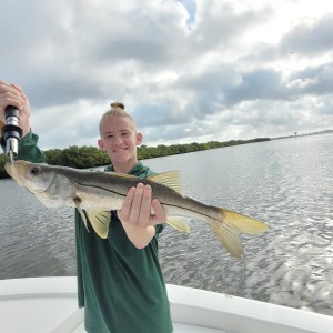Person holding a fish on a boat with water and cloudy sky in background.