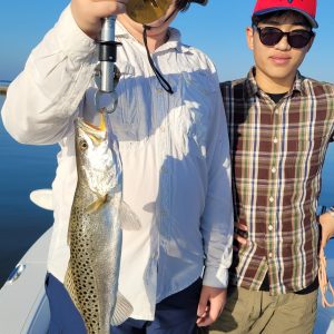 Two people on a boat holding a spotted fish.
