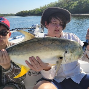 Two people on a boat holding a large fish, with a river and trees in the background.