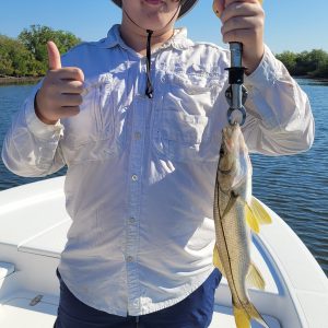 Person holding a fish on a boat, wearing a sun hat and giving a thumbs-up.