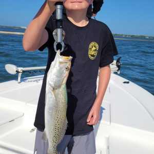 Boy on boat holding a fish with a gripping tool, water in background.