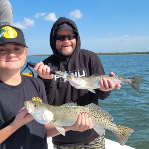 Two people holding caught fish on a boat in sunny weather.