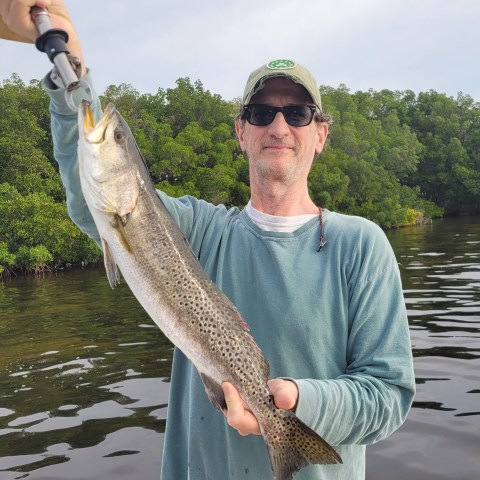 Person holding a large fish with greenery and water in the background.