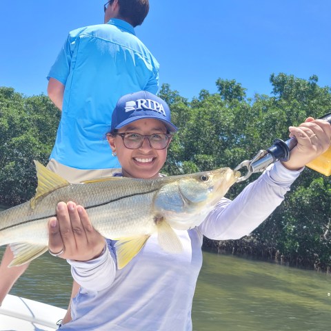 Person in cap smiling, holding a fish on a boat in sunny weather.