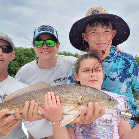 Group of four holding a large fish on a boat against a backdrop of greenery.