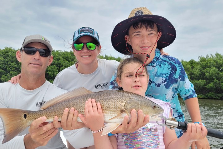 Group of four holding a large fish on a boat against a backdrop of greenery.