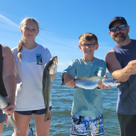 Four people holding fish on a boat under a clear blue sky.