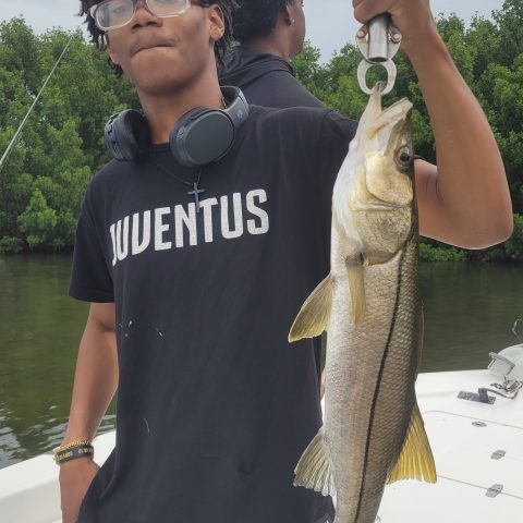 Person in glasses holding a fish on a boat with trees in the background.
