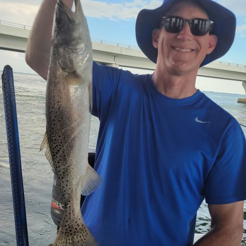 Man in blue shirt and hat holding a fish on a boat.