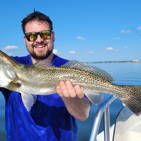 Man holding a large fish on a boat under a clear blue sky.