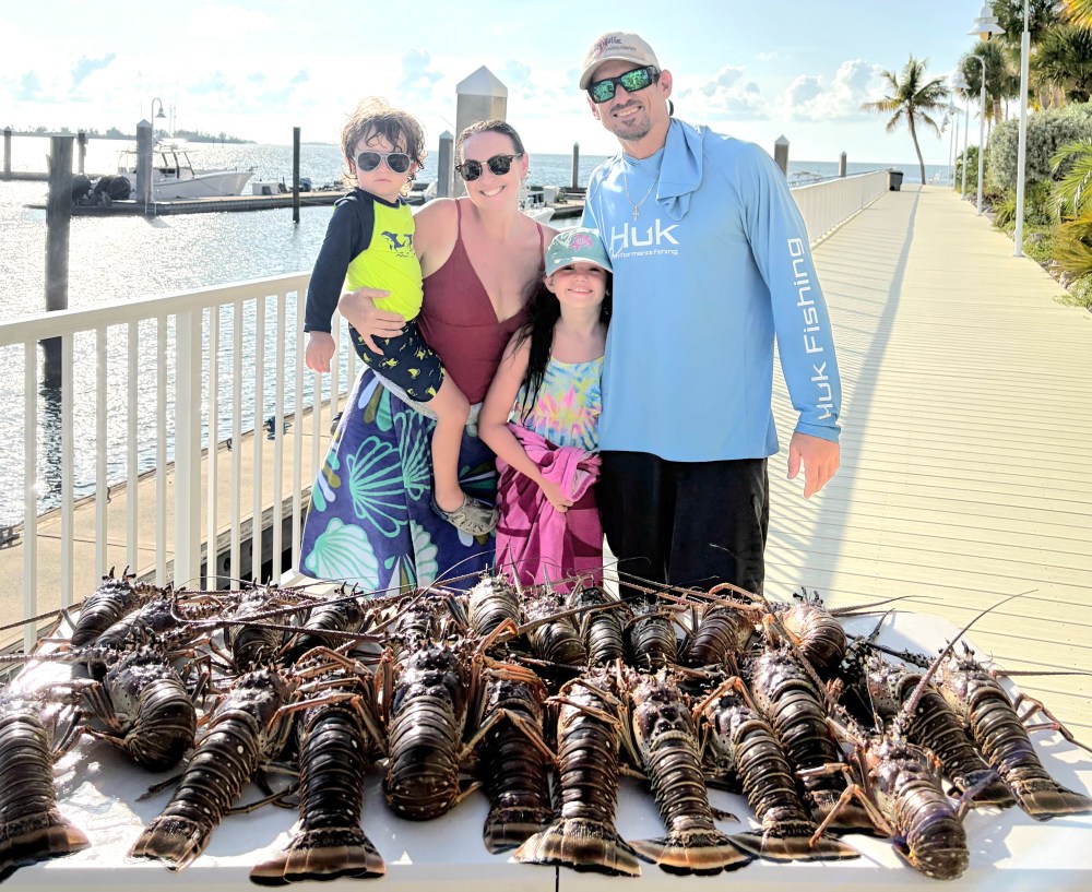 Family posing with lobsters on a dock by the water.
